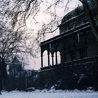 Snowy scene with a building and bare trees.