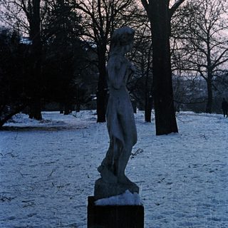 Statue stands in snowy park beneath twilight sky.