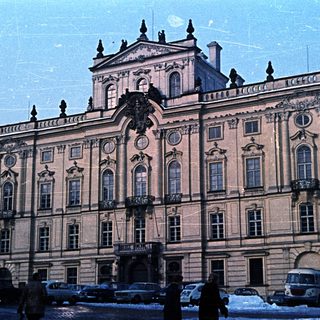 Ornate palace facade with winter scenery and vintage vehicles.