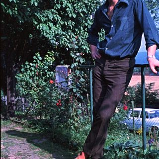 Man in casual wear stands in a garden setting.