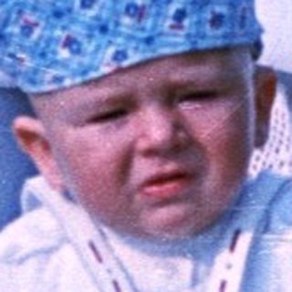 Baby in a vintage stroller sits outdoors, looking upset.