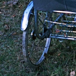 Baby in a vintage stroller sits outdoors, looking upset.
