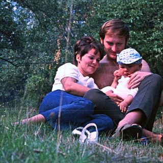 Couple sits in grass, embracing a baby outdoors.