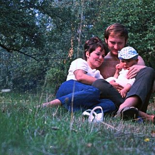 Couple sits in grass, embracing a baby outdoors.