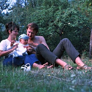 Couple with baby relaxing in a grassy, wooded area.
