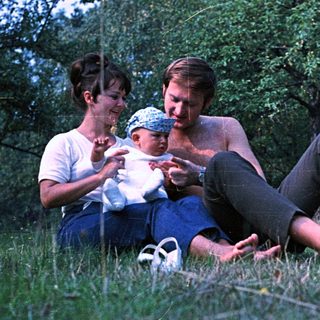 Couple with baby relaxing in a grassy, wooded area.