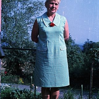 Woman in a checkered dress stands in a garden.