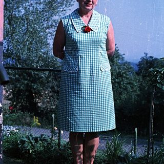 Woman in a checkered dress stands in a garden.