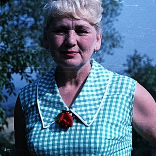 Woman in green dress smiles outdoors, standing near foliage.