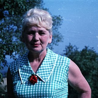 Woman in green dress smiles outdoors, standing near foliage.