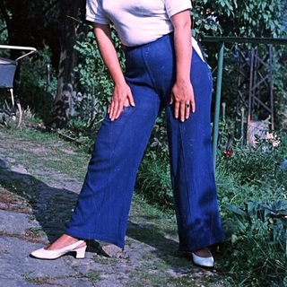 Woman in wide-leg pants stands outdoors in a garden.