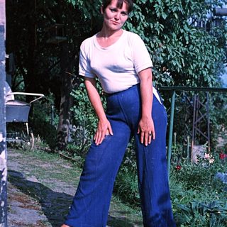 Woman in wide-leg pants stands outdoors in a garden.