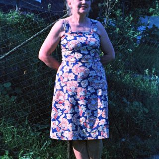 Woman in floral dress stands in a grassy yard.