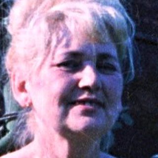 Woman in floral dress stands in a grassy yard.