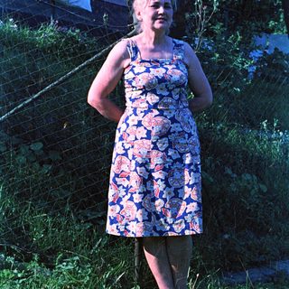 Woman in floral dress stands in a grassy yard.