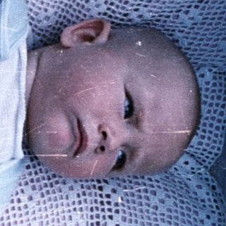 Baby lying in a crib with a blue pacifier.