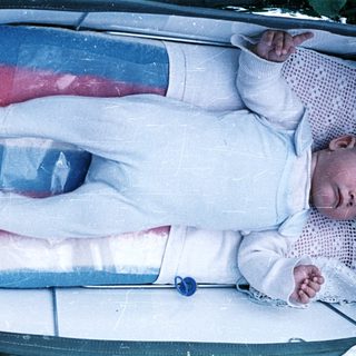 Baby lying in a crib with a blue pacifier.