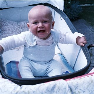 Baby in a stroller smiles, looking directly at the camera.