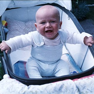 Baby in a stroller smiles, looking directly at the camera.