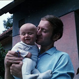 Man holds baby, smiling, in an outdoor setting.