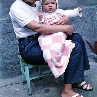 Woman sits with baby, wrapped in a pink blanket.