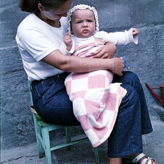 Woman sits with baby, wrapped in a pink blanket.