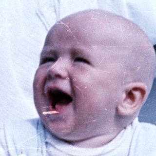 Baby in a high chair, appearing to cry or laugh.