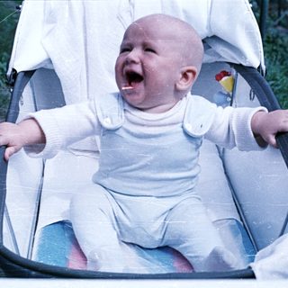 Baby in a high chair, appearing to cry or laugh.