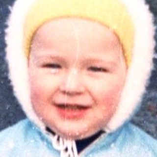 Young child stands on a snowy path wearing winter clothing.