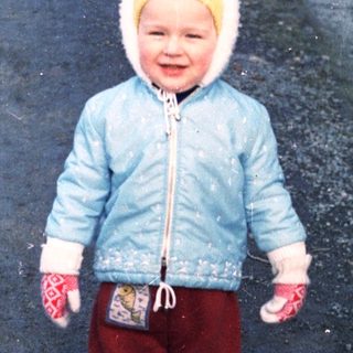 Young child stands on a snowy path wearing winter clothing.