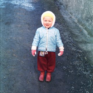 Young child stands on a snowy path wearing winter clothing.