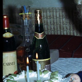 Baby held by woman near birthday cake and drinks.
