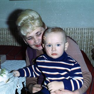 Baby held by woman near birthday cake and drinks.