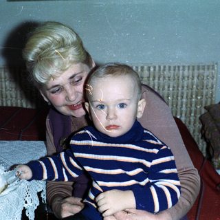 Baby held by woman near birthday cake and drinks.