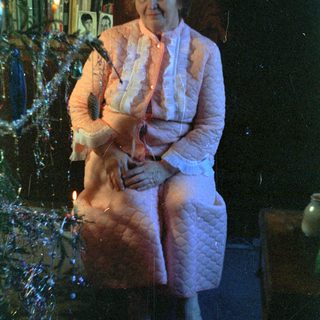 Here's a brief summary of the image: Woman in pink quilted suit sits near a fireplace.
