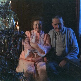 Couple sits before a brightly decorated Christmas tree.