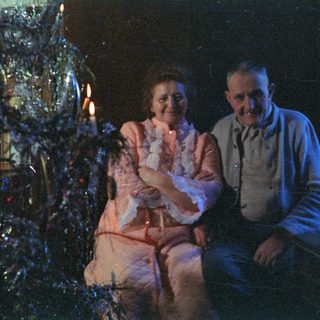 Couple sits before a brightly decorated Christmas tree.
