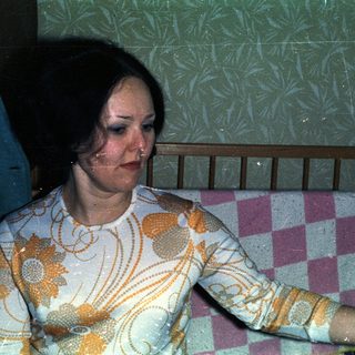 Woman seated near crib, wearing patterned top.