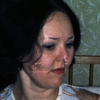 Woman seated near crib, wearing patterned top.