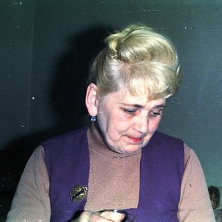 Here's a brief summary of the image: Woman with blonde hair is looking down, indoors.