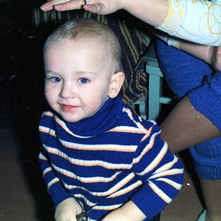 Baby in a striped sweater sits near a person.