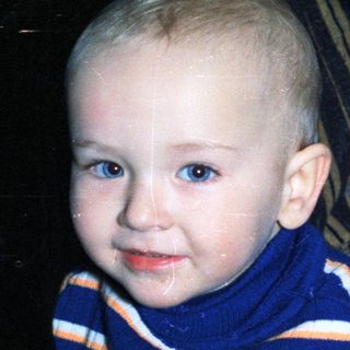 Baby in a striped sweater sits near a person.