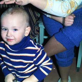 Baby in a striped sweater sits near a person.