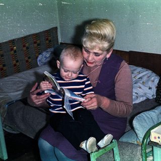 Woman reading to a young boy in a bedroom.