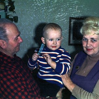 Baby being held by grandparents in a vintage-style portrait.