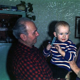 Baby being held by grandparents in a vintage-style portrait.