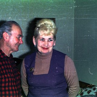 Couple poses indoors, smiling, in a vintage-style setting.