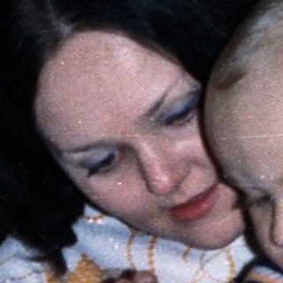 Woman holds baby, birthday cake and drinks are present.