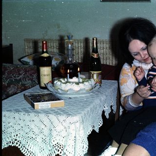 Woman holds baby, birthday cake and drinks are present.