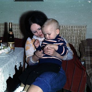 Woman holds baby, birthday cake and drinks are present.